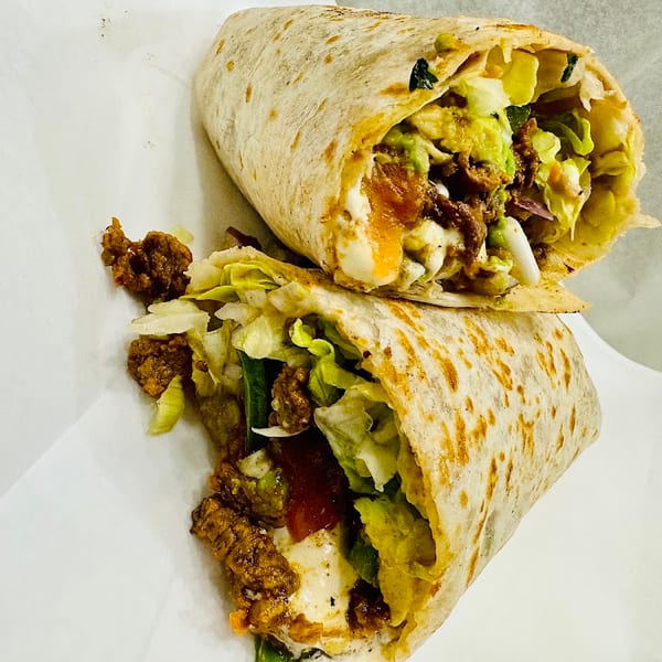 Two hearty wraps filled with seasoned meat, lettuce, avocado, and creamy sauce, served in white paper.