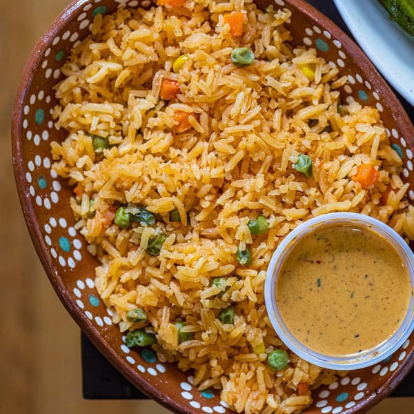 Mexican rice with peas, carrots, and corn in a decorative bowl with a side of sauce.