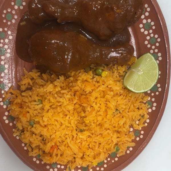 Two chicken drumsticks in mole sauce with a side of orange rice and a lime wedge.