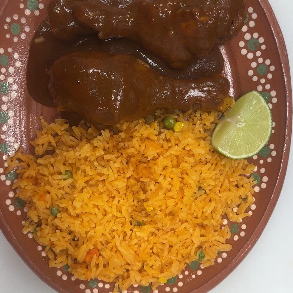 Two chicken drumsticks in mole sauce with a side of orange rice and a lime wedge.