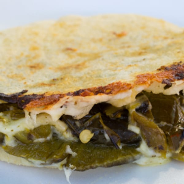 A close-up of a quesadilla filled with melted cheese and green poblano peppers.