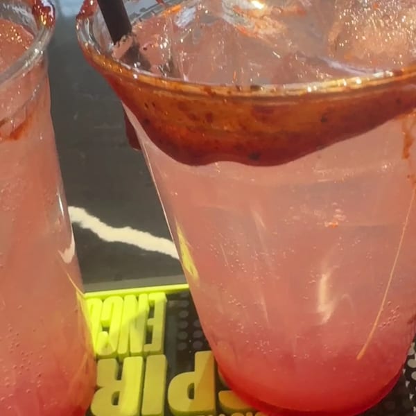 Two pink drinks with ice and chili-lime rims sit on a black bar mat.