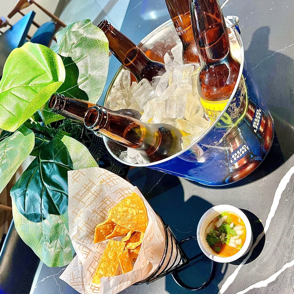 Ice bucket of beers with tortilla chips and salsa on a sunny table.